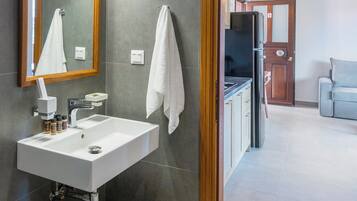 A modern bathroom with a white sink, wooden bench, and a large mirror.