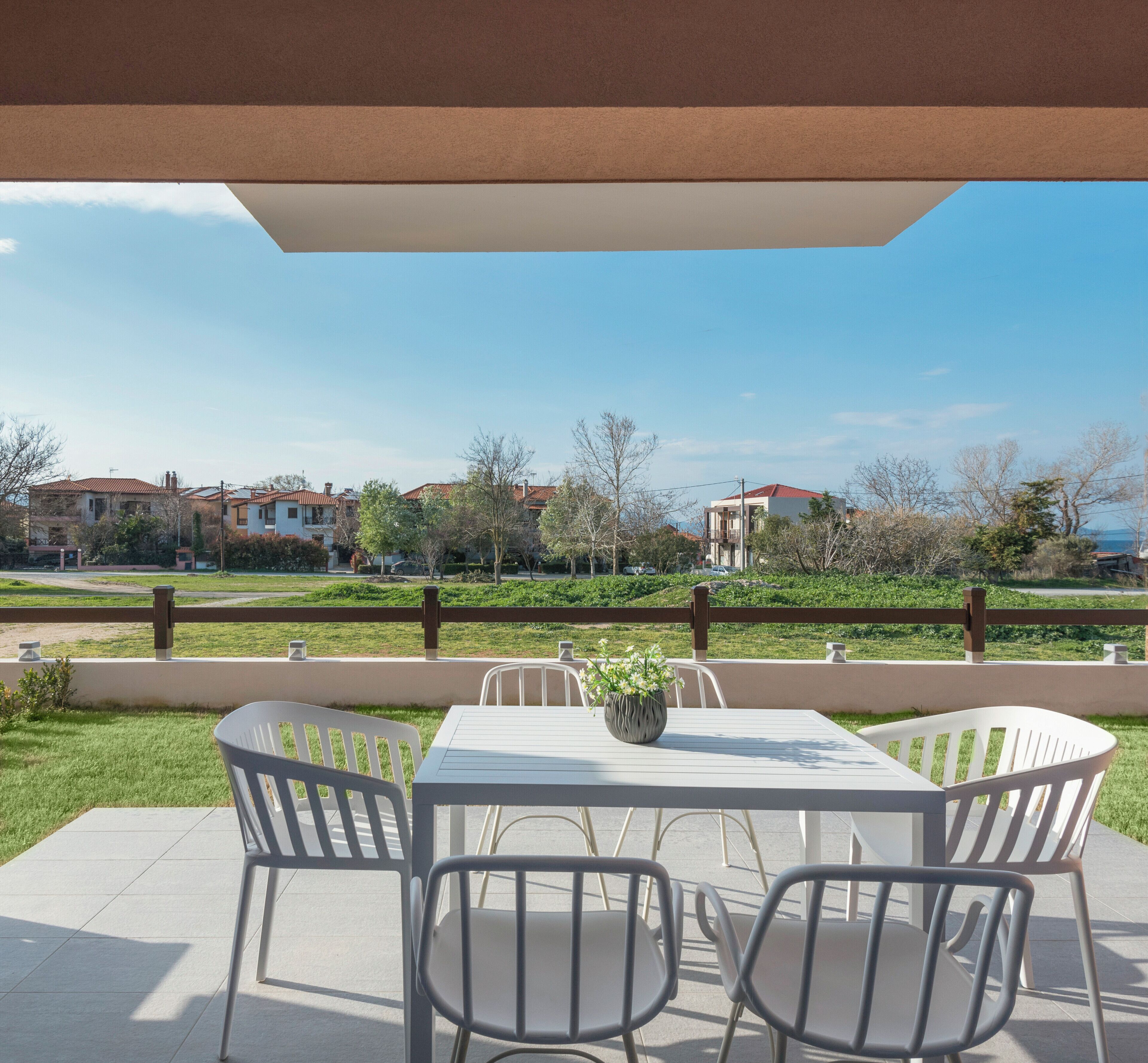 An outdoor patio with a table and chairs, a potted plant, and a view of houses and greenery.