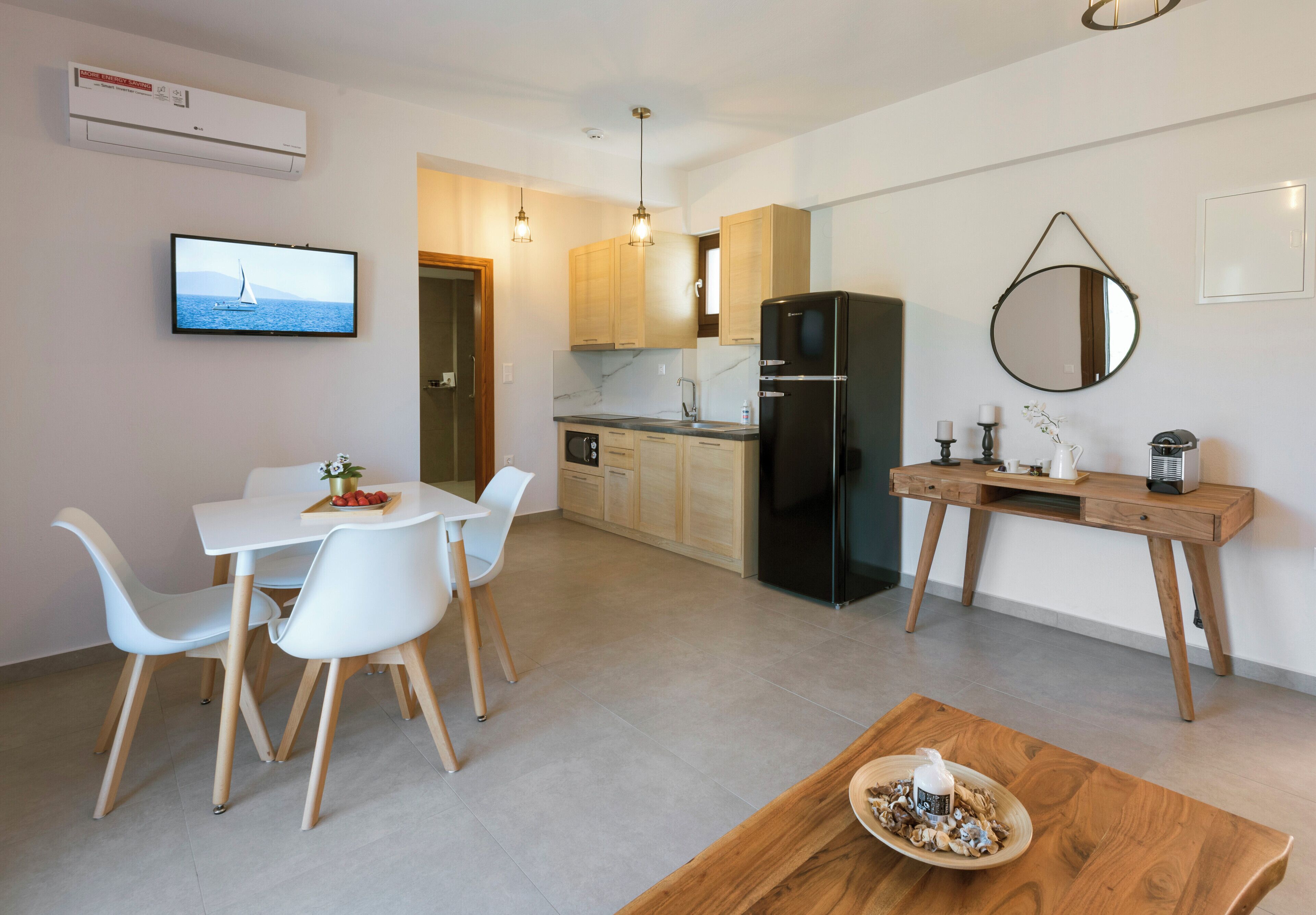 Una cocina moderna con un refrigerador negro, armarios de madera y un comedor con sillas blancas y una mesa de madera.