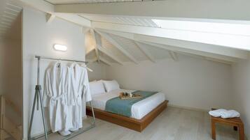 Un dormitorio con techo inclinado, estructura de cama de madera, mesita de noche y perchero con batas blancas.