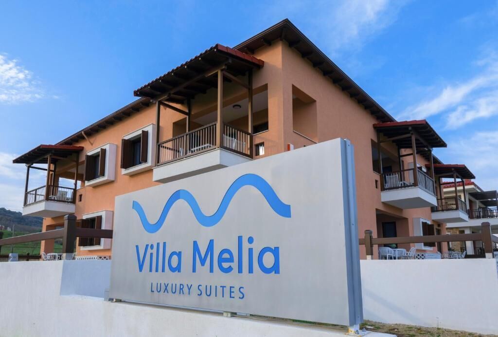 A sign for Villa Melia Luxury Suites with a modern building in the background.