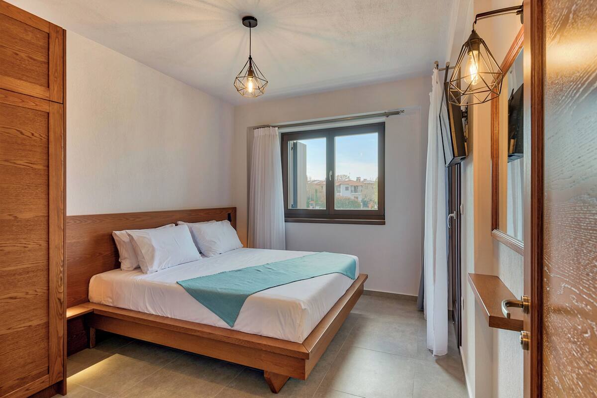 Ein Schlafzimmer mit einem hölzernen Bett, einem Fenster mit Vorhängen und Blick auf Gebäude.