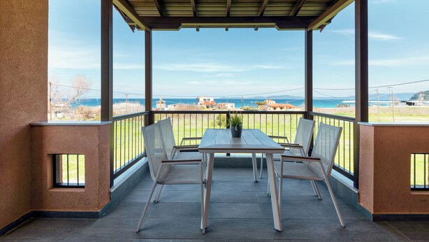 Een overdekt balkon met een tafel en stoelen, met uitzicht op een prachtig zeegezicht en verre gebouwen.