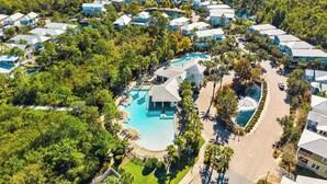 Een luchtendicht van een resort met meerdere gebouwen, een centraal zwembad en omliggend groen.