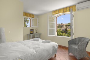 A bedroom with a bed, a chair, a desk, and a window with a view of buildings. - Villa Marie – Views & Pool in Vence (Vence)