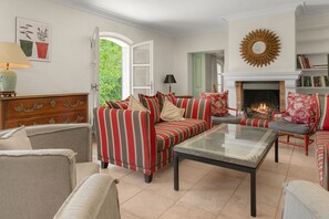 A living room with a striped sofa, a glass coffee table, and a fireplace. - Villa Marie – Views & Pool in Vence (Vence)