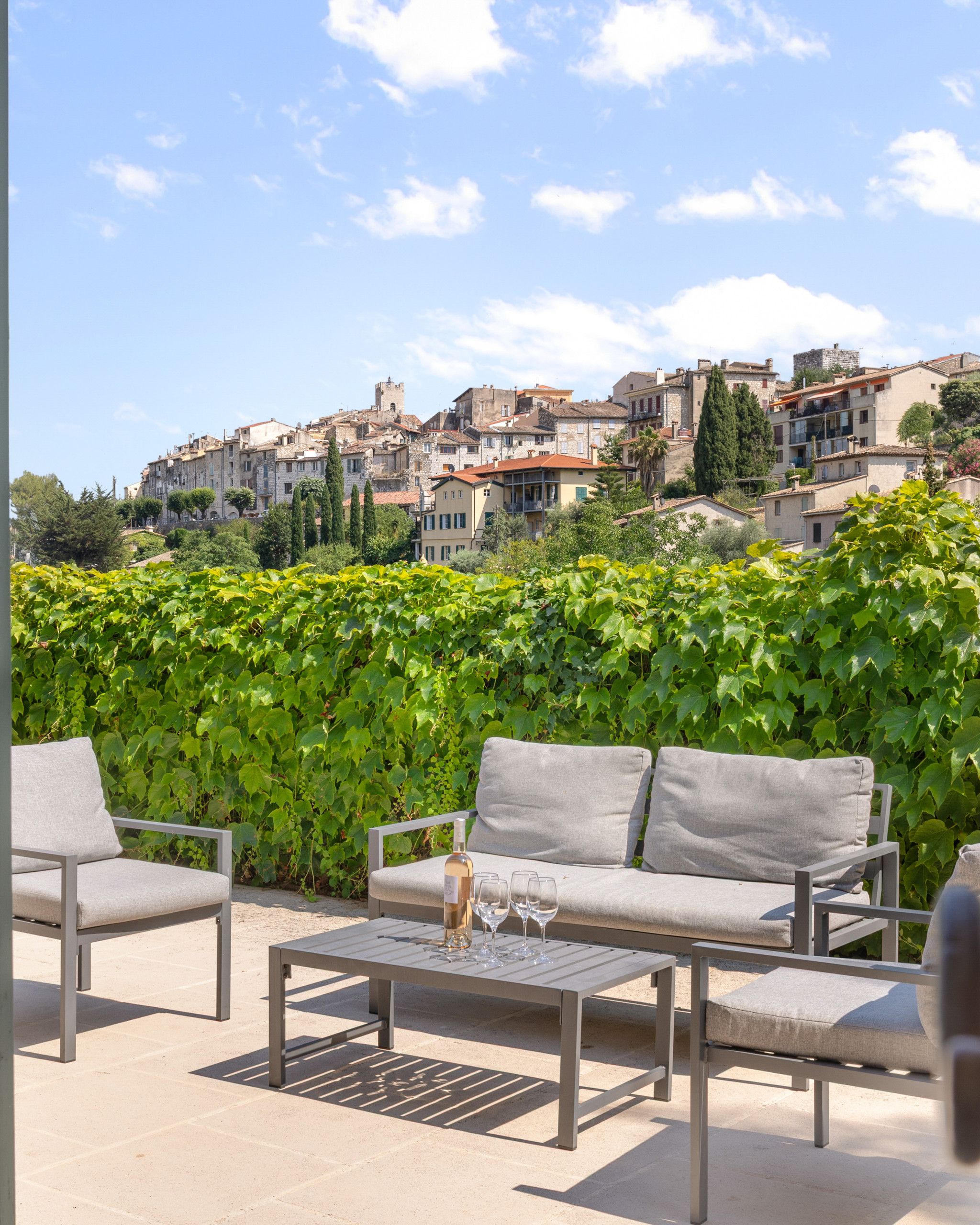 An outdoor seating area with a table and chairs, a bottle of wine, and a view of a historic town with buildings and a tower.