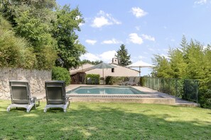 A backyard with a swimming pool, two lounge chairs, a patio umbrella, and a stone wall. - Villa Marie – Views & Pool in Vence (Vence)