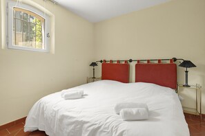 A neatly made bed with white linens and two rolled towels, a window with a view of greenery, and a bedside table with a lamp. - Villa Marie – Views & Pool in Vence (Vence)