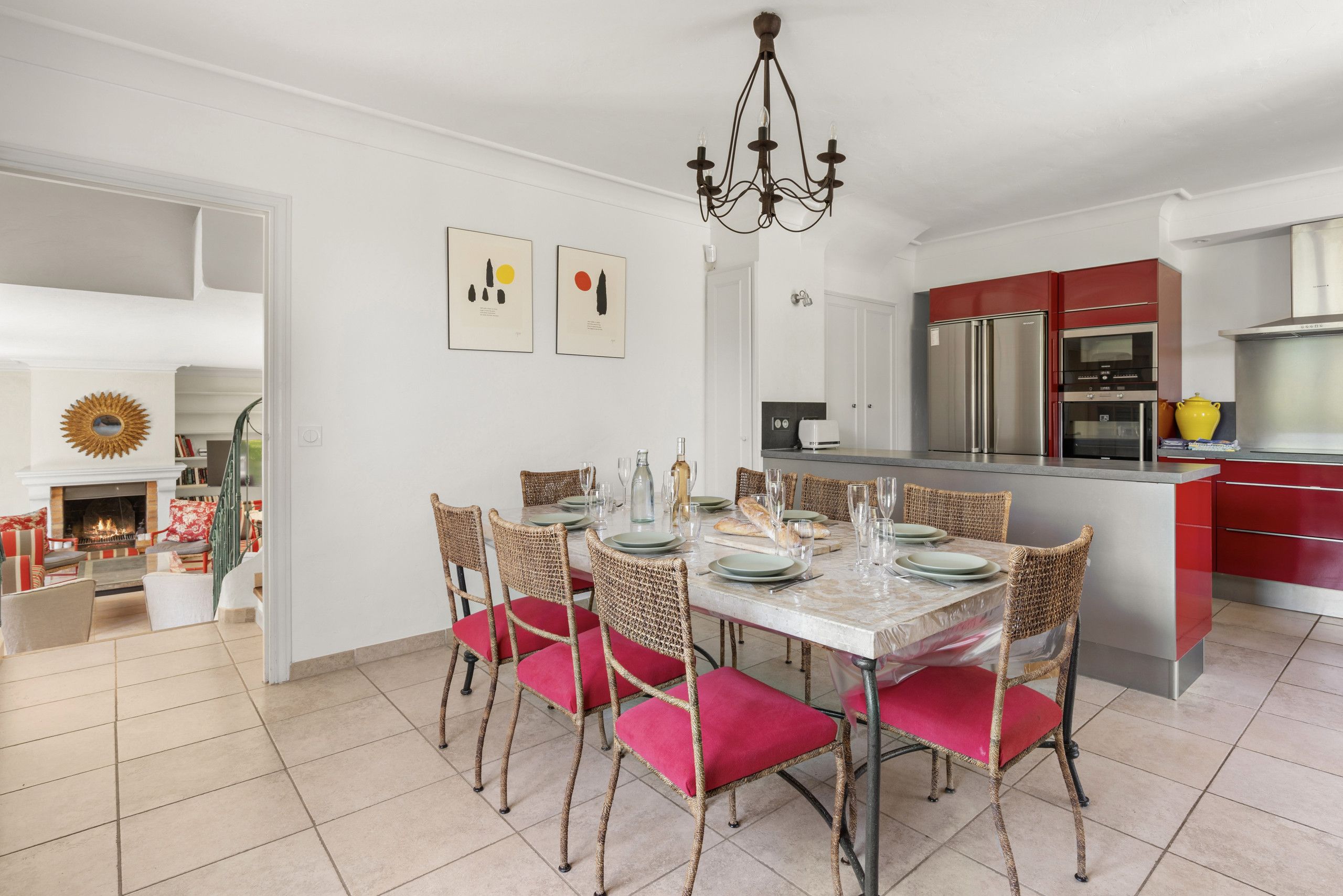 A modern kitchen with red cabinets, a stainless steel refrigerator, and a dining area with a white table set for six.