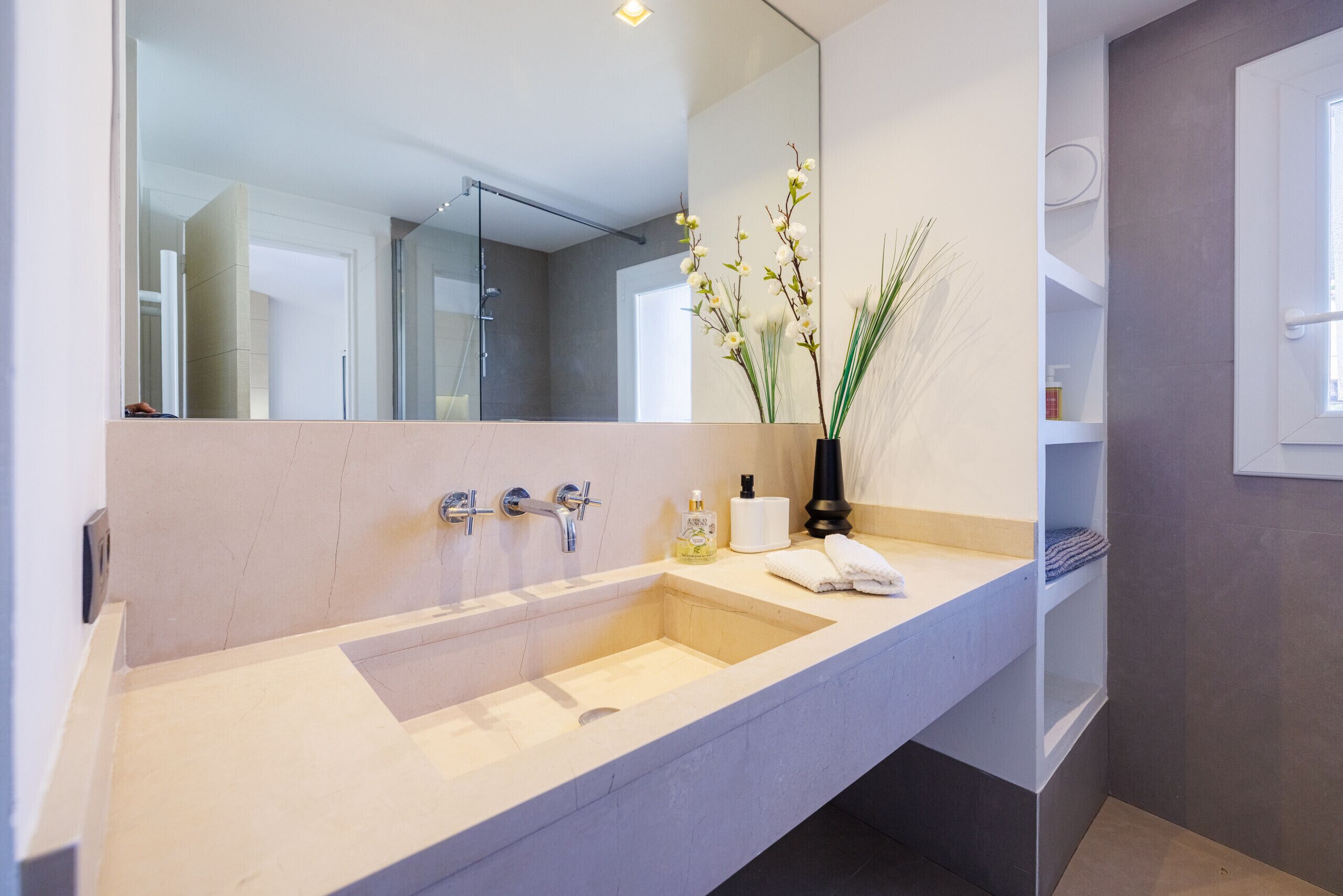 Une salle de bain moderne avec un grand lavabo, un miroir et un vase rempli de fleurs.