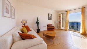 A living room with a sofa, a coffee table, a cactus, a chair, and a balcony with a view. - Apt le NID - Sea view in the village (Tourrettes-sur-Loup)