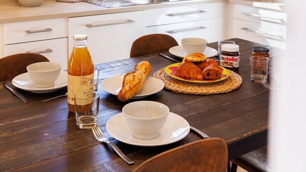 A dining area with a table set for breakfast, including croissants, a bottle of juice, and a glass of water. - Apt le NID - Sea view in the village (Tourrettes-sur-Loup)