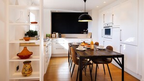 A modern kitchen with white cabinetry, a wooden dining table, and a black pendant light. - Apt le NID - Sea view in the village (Tourrettes-sur-Loup)