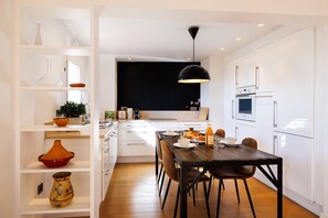 A modern kitchen with white cabinetry, a wooden dining table, and a black pendant light. - Apt le NID - Sea view in the village (Tourrettes-sur-Loup)