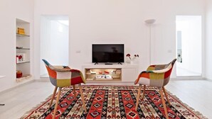 A modern living room with a flat-screen TV, two colorful chairs, a patterned rug, and a white entertainment unit. - SUITE BOSCHETTO HOLIDAYS, warm apartment in the historic center of Rome (Roma)