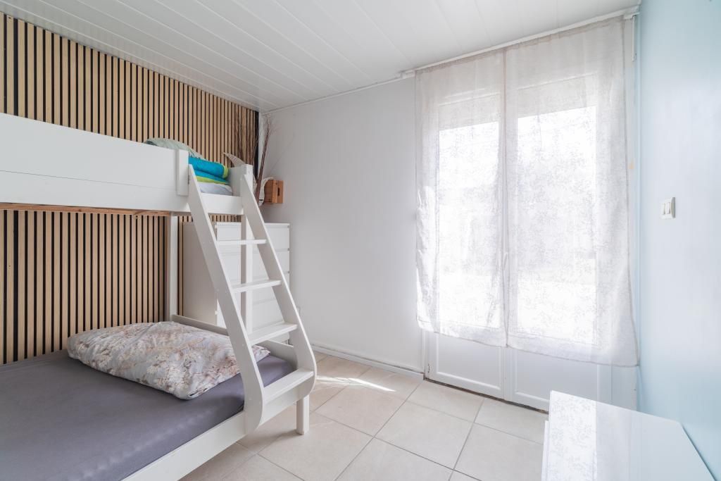 A room with a bunk bed, a ladder, a window with curtains, and a white wall.