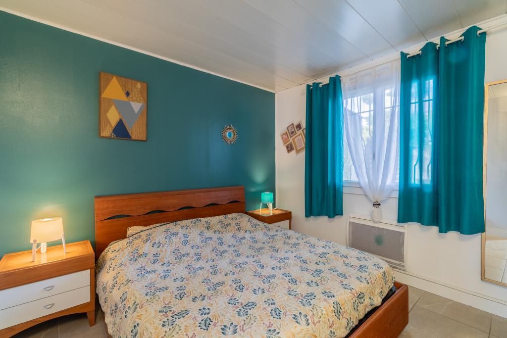 Quarto com cama, mesa de cabeceira, abajur, janela com cortinas e parede com pintura geométrica.