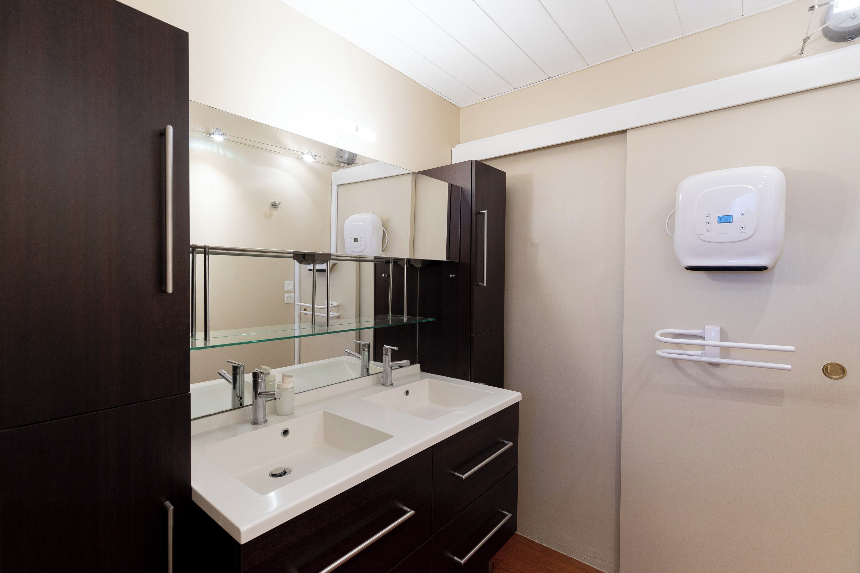 Een moderne badkamer met twee wasbakken, een grote spiegel en een handdoekdispenser.