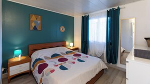 Une chambre bien rangée, avec un lit, des tables de chevet, une commode, un miroir et une fenêtre avec des rideaux.