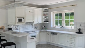 A modern kitchen with white cabinetry, a built-in oven, and a window with a view of greenery. - Spacious vacation bungalow in Scharbeutz (125sqm) (Scharbeutz)