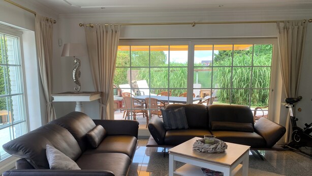 A modern living room with two leather sofas, a coffee table, and a view of the outdoors through large windows. - Spacious vacation bungalow in Scharbeutz (125sqm) (Scharbeutz)