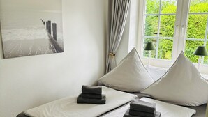 A neatly made bed with grey linens and pillows, a wooden headboard, and a window with curtains. - Spacious vacation bungalow in Scharbeutz (125sqm) (Scharbeutz)