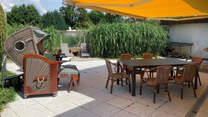 A patio with a dining table, chairs, a small water feature, and a yellow canopy. - Spacious vacation bungalow in Scharbeutz (125sqm) (Scharbeutz)