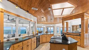 Une cuisine spacieuse dotée de meubles en bois, d’un grand îlot central et offrant une vue sur la mer.
