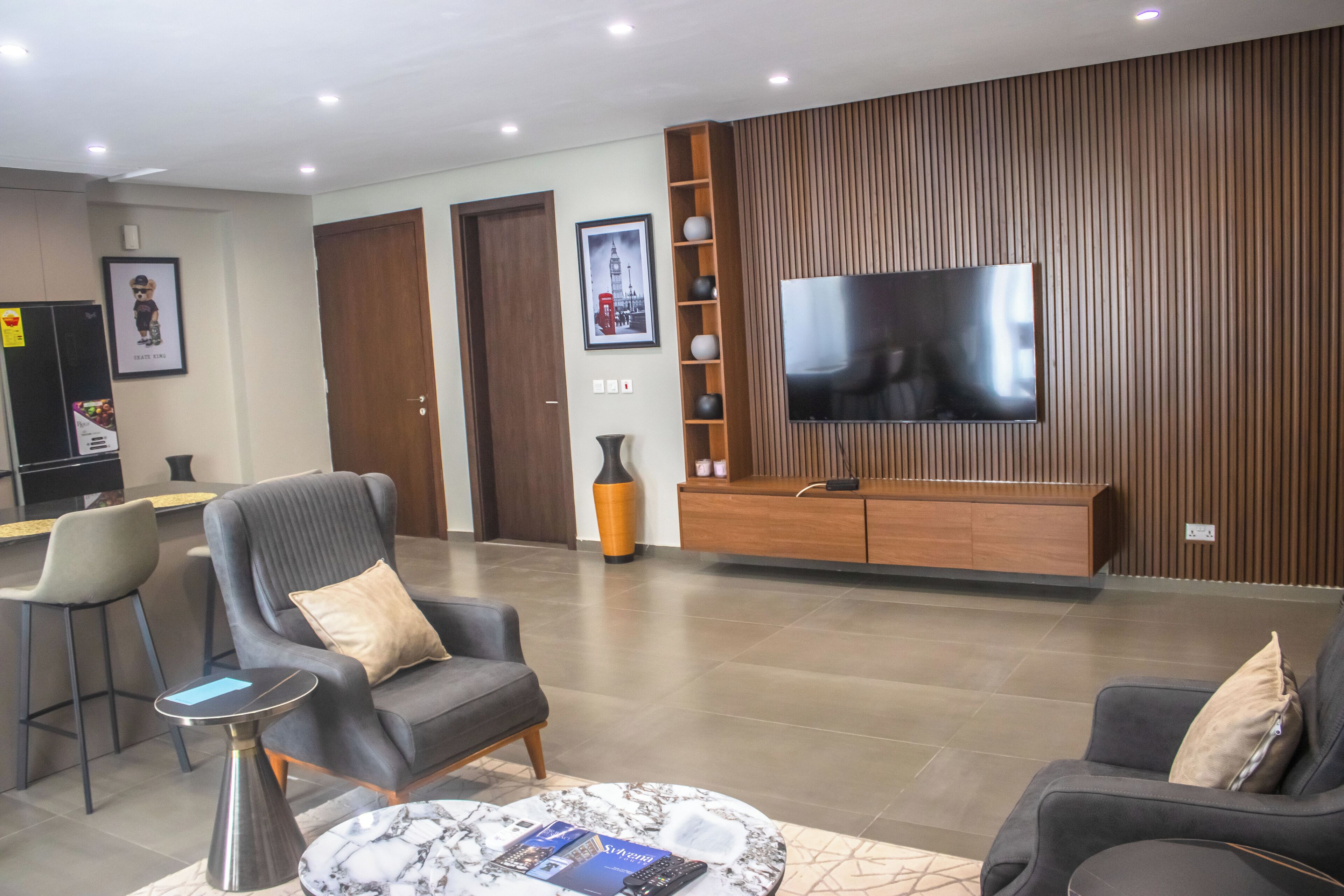 Una sala de estar moderna con un televisor de pantalla plana, sofás grises, una mesa de centro y un panel de pared de madera.