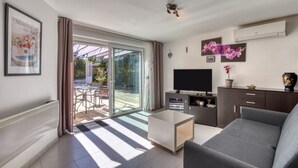 Una sala de estar moderna con un sofá, televisión y puerta corrediza de vidrio que da a un espacio exterior.
