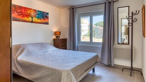 Un dormitorio con cama, un cuadro, una ventana con cortinas, un radiador y un perchero.