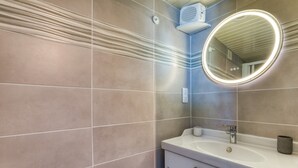 Un baño con un lavamanos blanco, un espejo redondo con luz y un perchero para toallas.