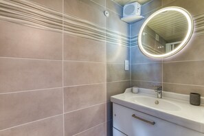 A bathroom with a white sink, a round mirror with a light, and a towel rack. - Le Jardin de Benjamin: Comfortable Apartment with Pool (Montagnac)