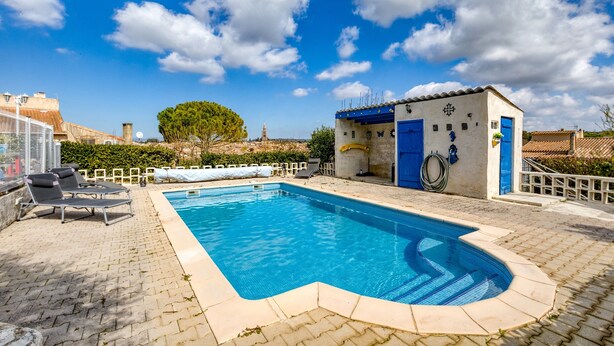 Una piscina con sillas de descanso, un edificio pequeño con puertas azules y un cielo despejado.