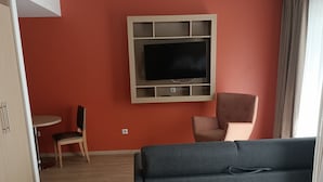 Une chambre d’hôtel comprenant un lit, un canapé, un téléviseur fixé au mur, un bureau avec une chaise et une fenêtre avec des rideaux.