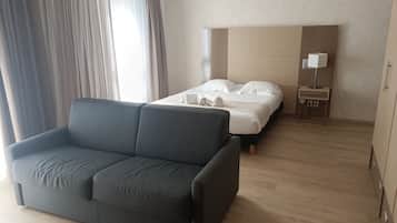 Une chambre d’hôtel avec un canapé, un lit avec du linge de maison blanc, une table de chevet avec une lampe et un mur décoré d’un motif.