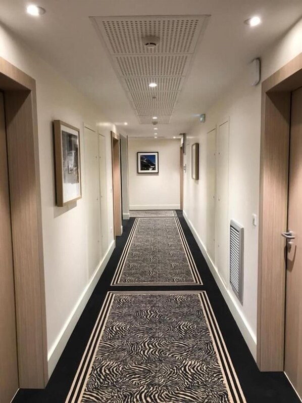 A hotel hallway with a black and white patterned carpet, wooden doors, and framed pictures on the walls.