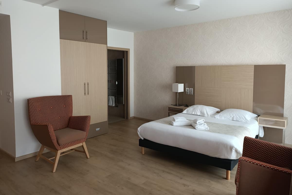 Una camera d'albergo con un letto, una sedia, un armadio, un comodino e una lampada.