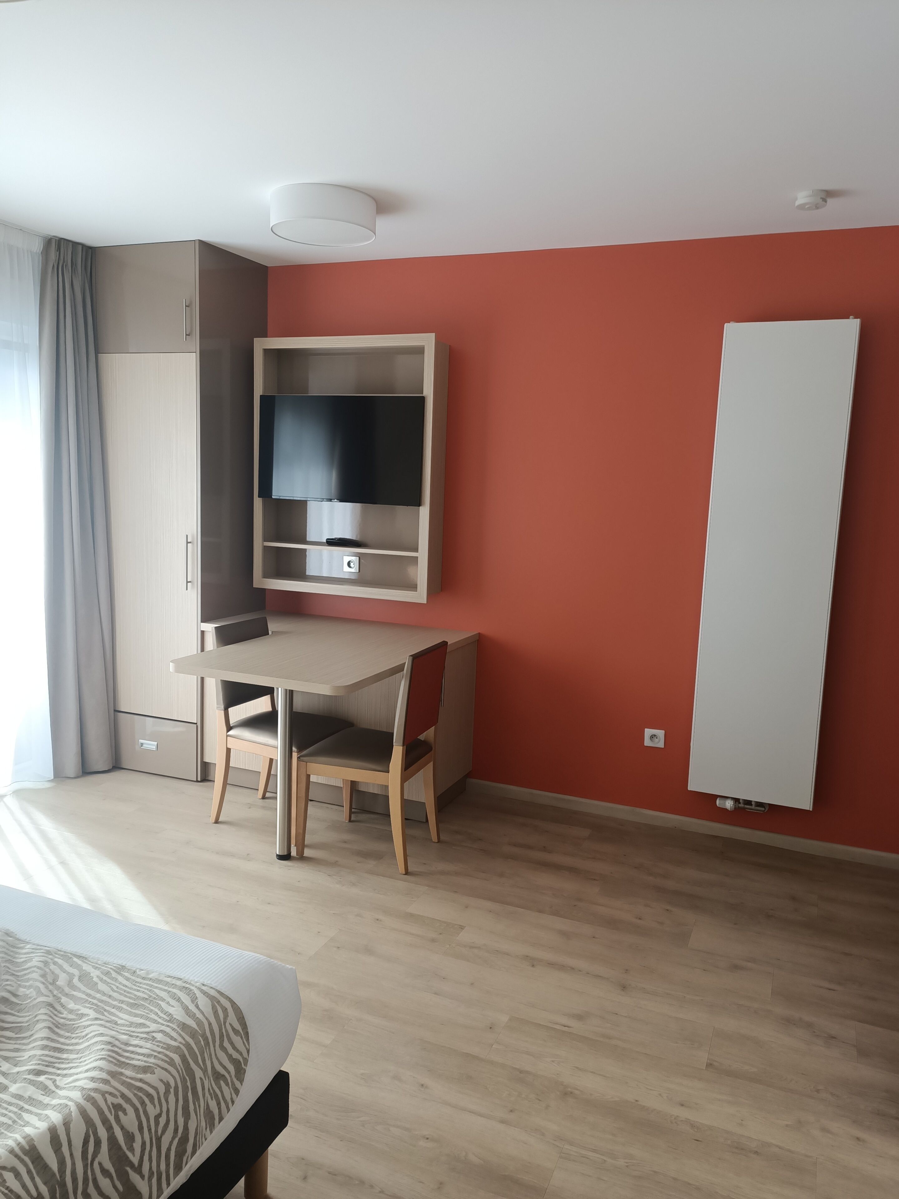 Een moderne kamer met een houten bureau, een flatscreen-tv, een bed met een beddegoed met een zebraprint en een rode accentmuur.