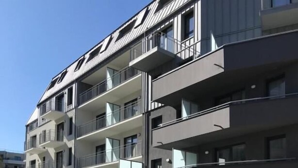 Un immeuble résidentiel à plusieurs étages, doté de balcons, d’une entrée sécurisée et d’un petit espace paysager avec des arbres.