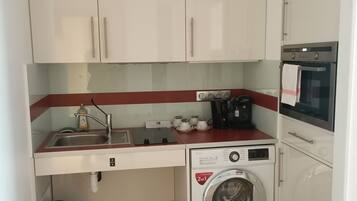Une cuisine de taille réduite, avec des meubles blancs, un lave-linge, un four à micro-ondes et un évier.
