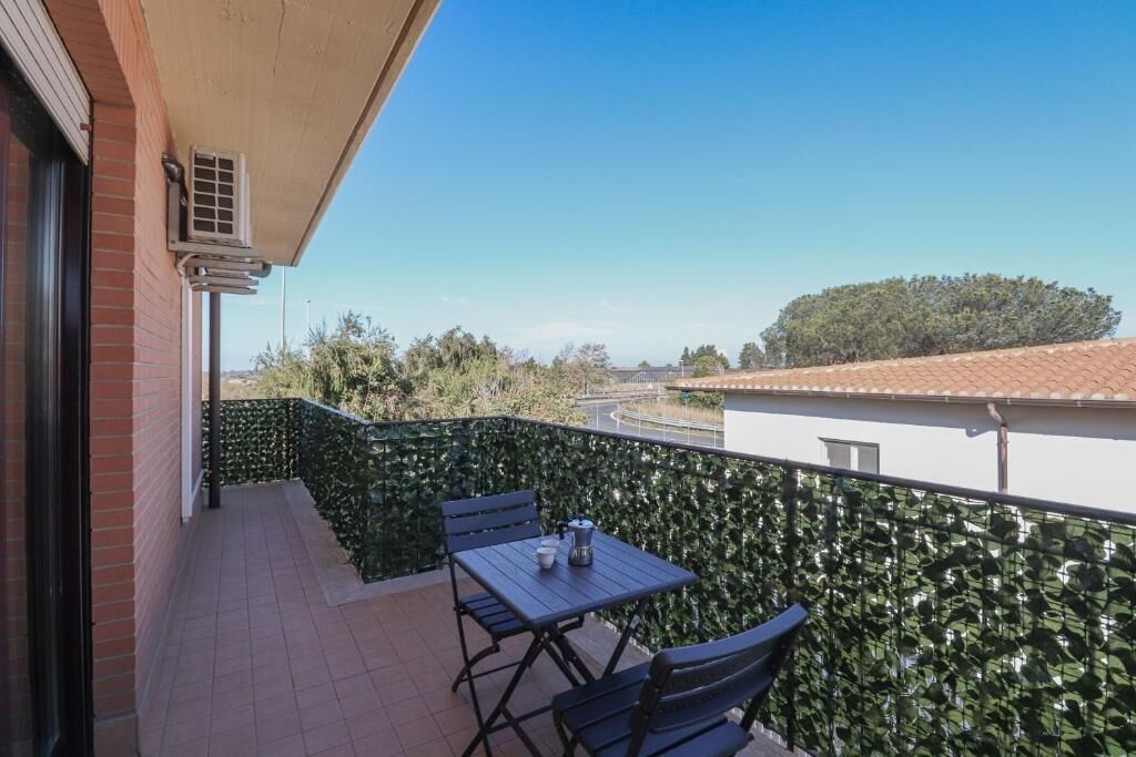A balcony with a table and chairs, a view of the street, and a hedge.