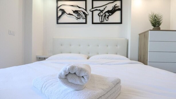 Ein ordentlich bezogenes Bett mit einem gefalteten Handtuch im Vordergrund, einem gebürsteten Kopfteil und zwei gerahmten Kunstwerken an der Wand.