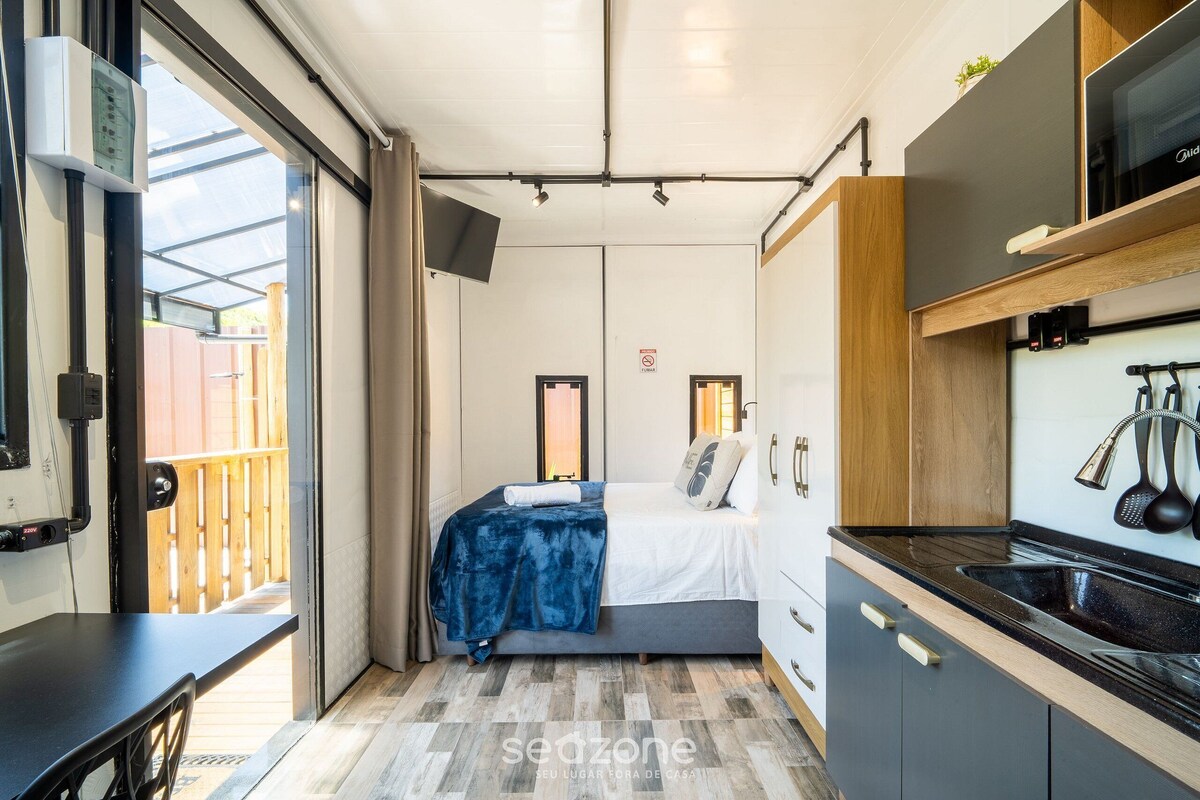 Une pièce compacte comprenant un lit, une petite kitchenette et une porte coulissante donnant sur un espace extérieur.