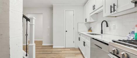 A modern kitchen with white cabinets, a stainless steel stove, and a wooden floor.