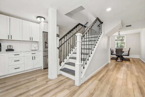 A modern kitchen with white cabinets, a stainless steel refrigerator, and a dining area with a table and chairs.