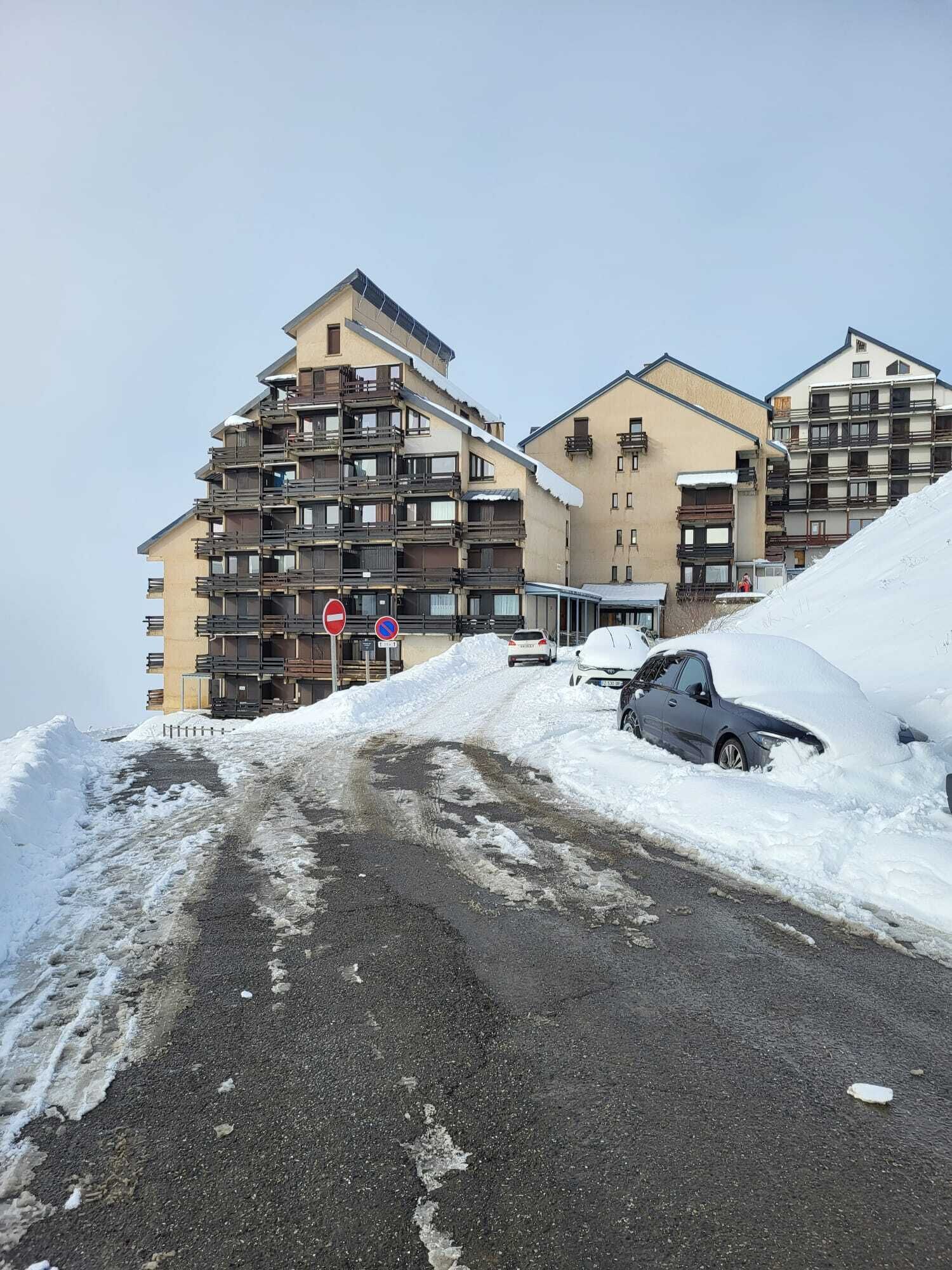 Um edifício com várias andares e varandas, um sinal de proibido estacionar e um carro parcialmente coberto pela neve.