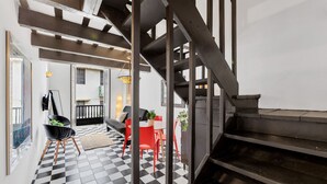Un intérieur moderne avec un sol à carreaux noir et blanc, un escalier et un coin repas avec des chaises rouges.