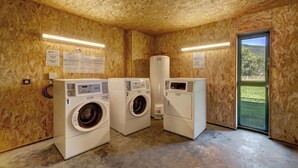 A laundry room with three white front-loading washing machines, wooden walls, and a large window with a view of greenery. - Vacancéole Les Chambres des Oiseaux (Motz)
